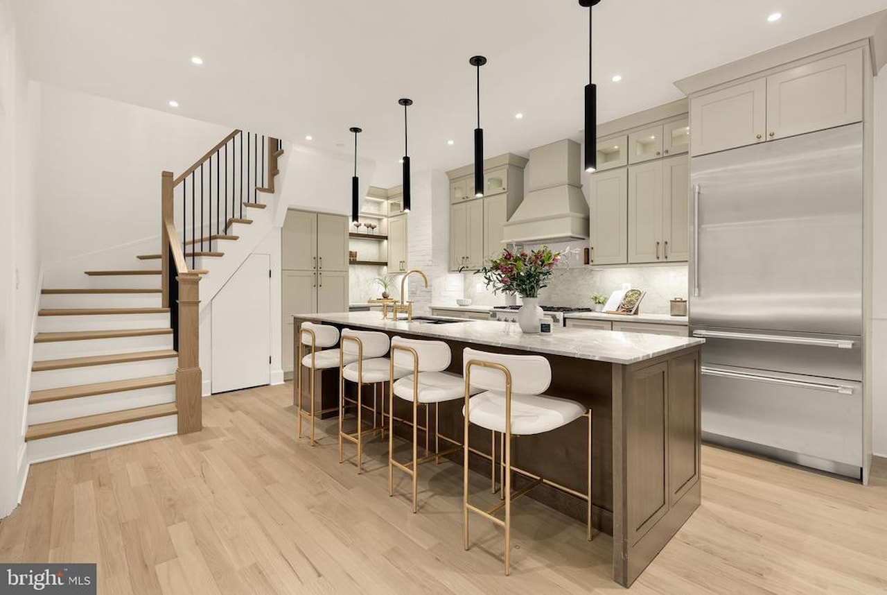 Kitchen with island, brass barstools, and staircase